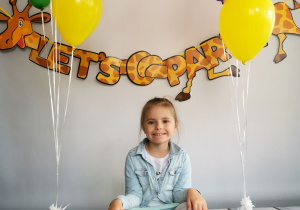 Dziewczynka siedzi na tle fotograficznym i pozuje do zdjęcia wśród balonów.
